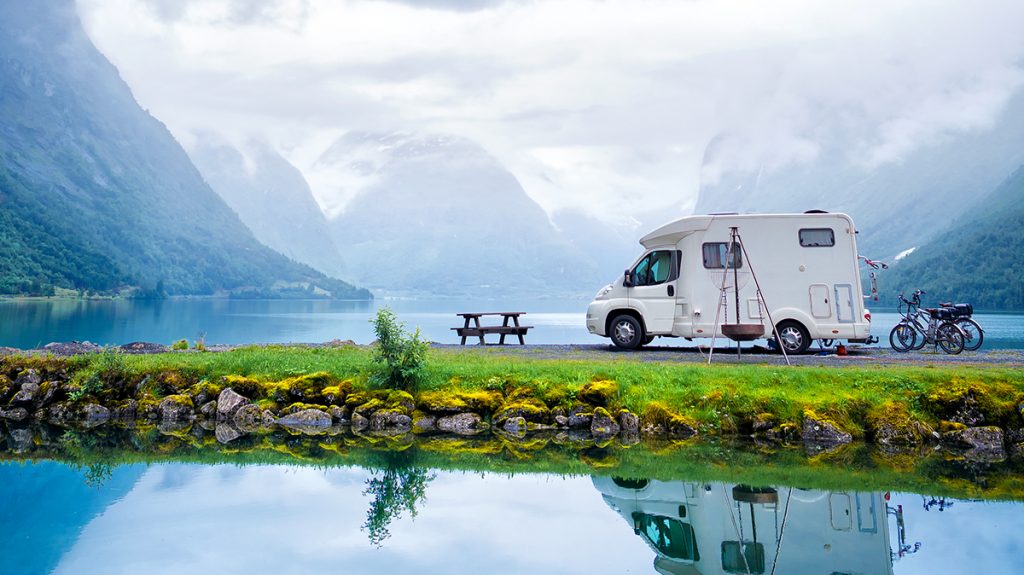 Camper in riva a un lago accanto una panchina di legno